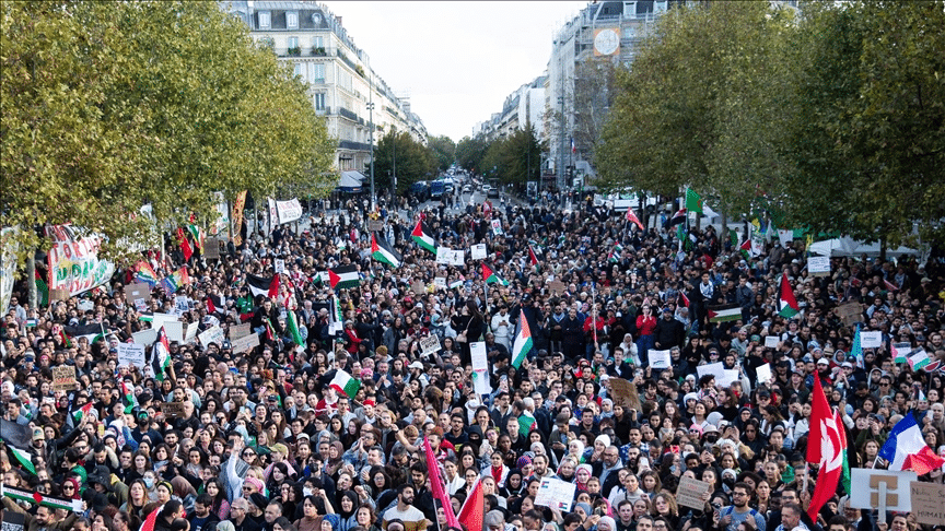 Dense crowd of pro-Palestinian demonstrators filling a wide city street, holding and waving many Palestinian flags.