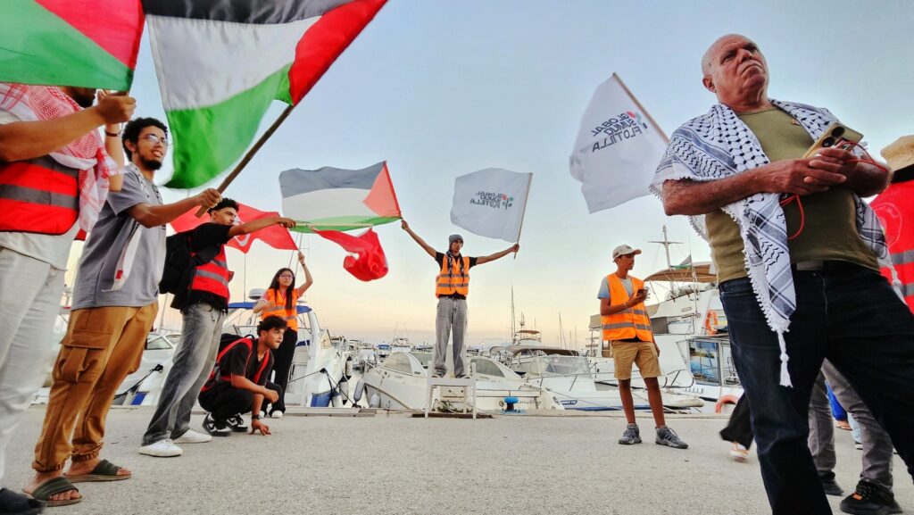 participant of global sumud flotilla standing and waving flags of palestine