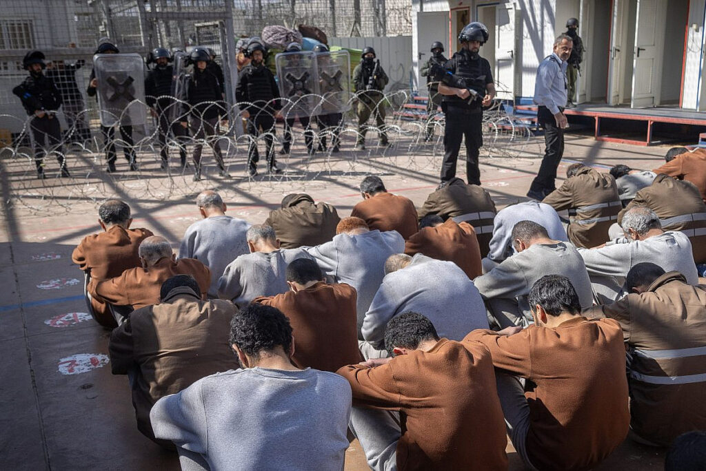 Palestinian hostages sitting in front of Israeli soldiers.