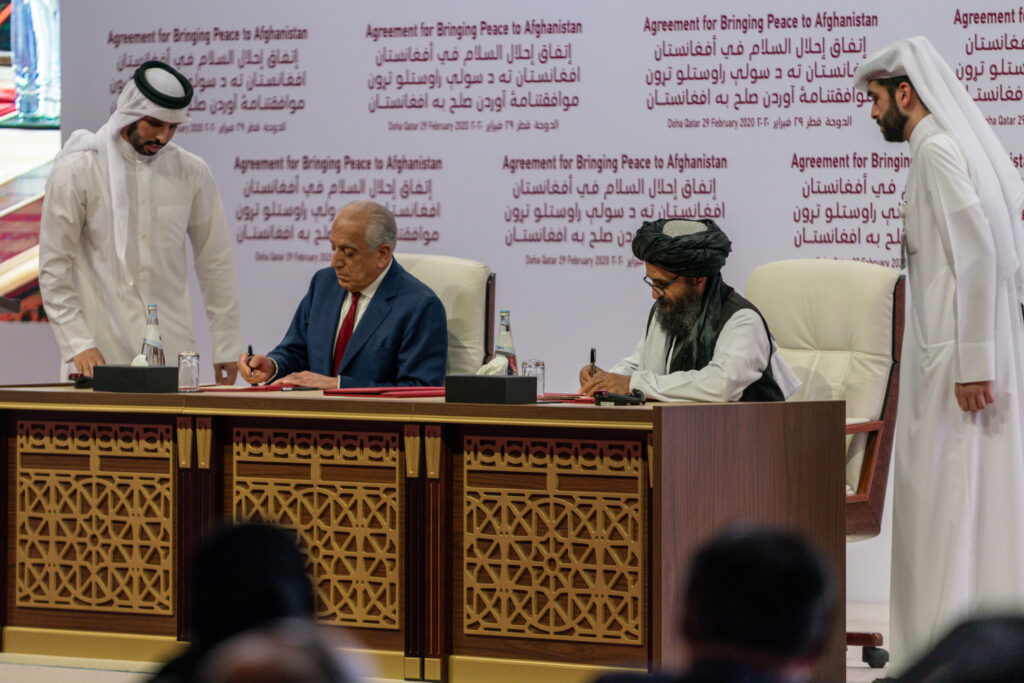 American diplomat Zalmay Khalilzad (left) and Taliban diplomat Abdul Ghani Baradar (right) signing the agreement in the presence of Qatari mediators at the Sheraton Grand Doha Resort